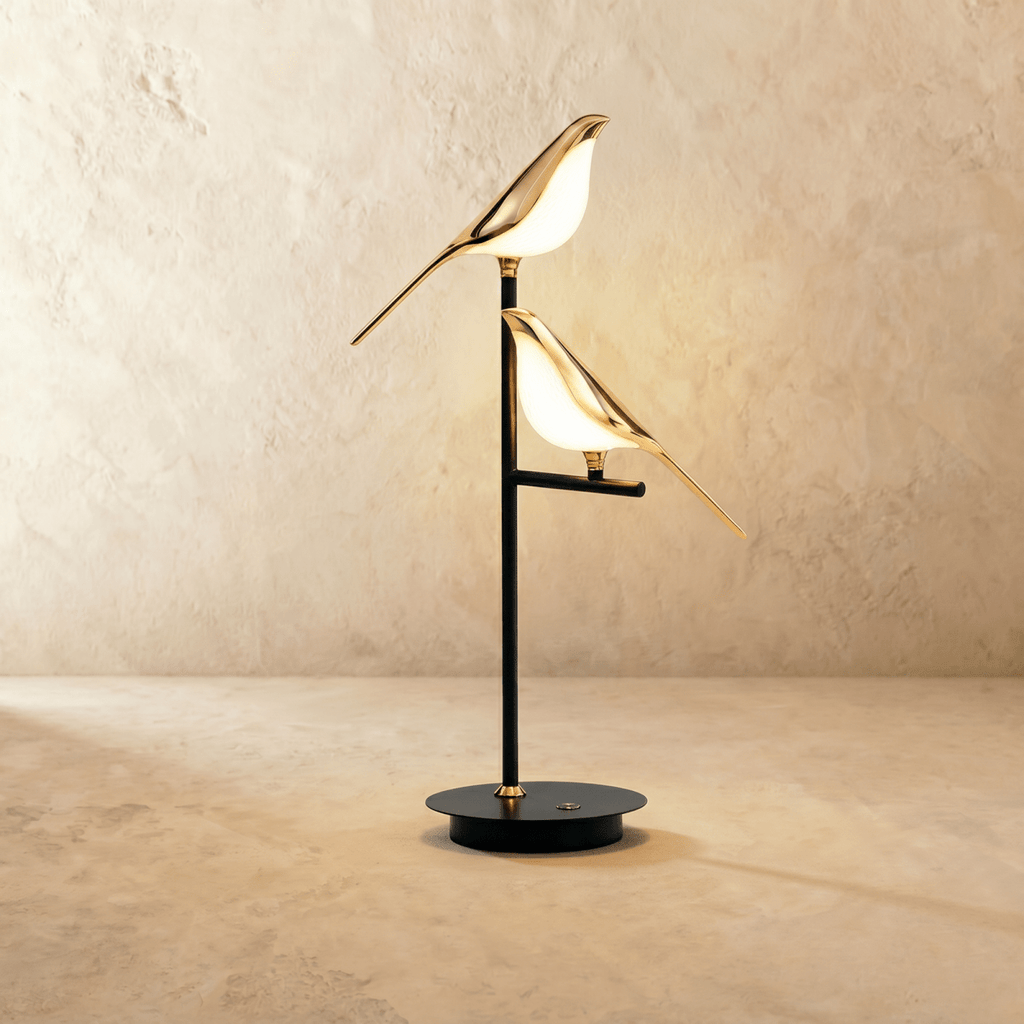 Clérachic two-head bird table lamp with two glowing gold birds perched at different heights on a black stem and round base.
