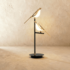 Clérachic two-head bird table lamp with two glowing gold birds perched at different heights on a black stem and round base.