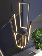 Clérachic staggered rectangular LED frames glowing warm white, seen from above in a stairwell with a potted plant below.