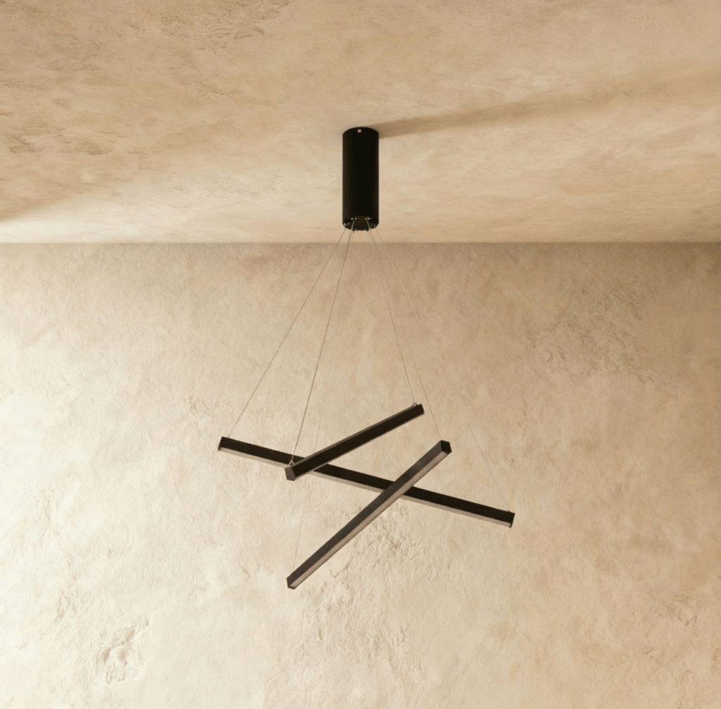 Another angle of the Clérachic black staggered chandelier, three crossed aluminium bars glowing warm white on thin cables.