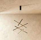 The Clérachic black chandelier with five crossed aluminium bars, each glowing warm white, suspended from a plastered ceiling.