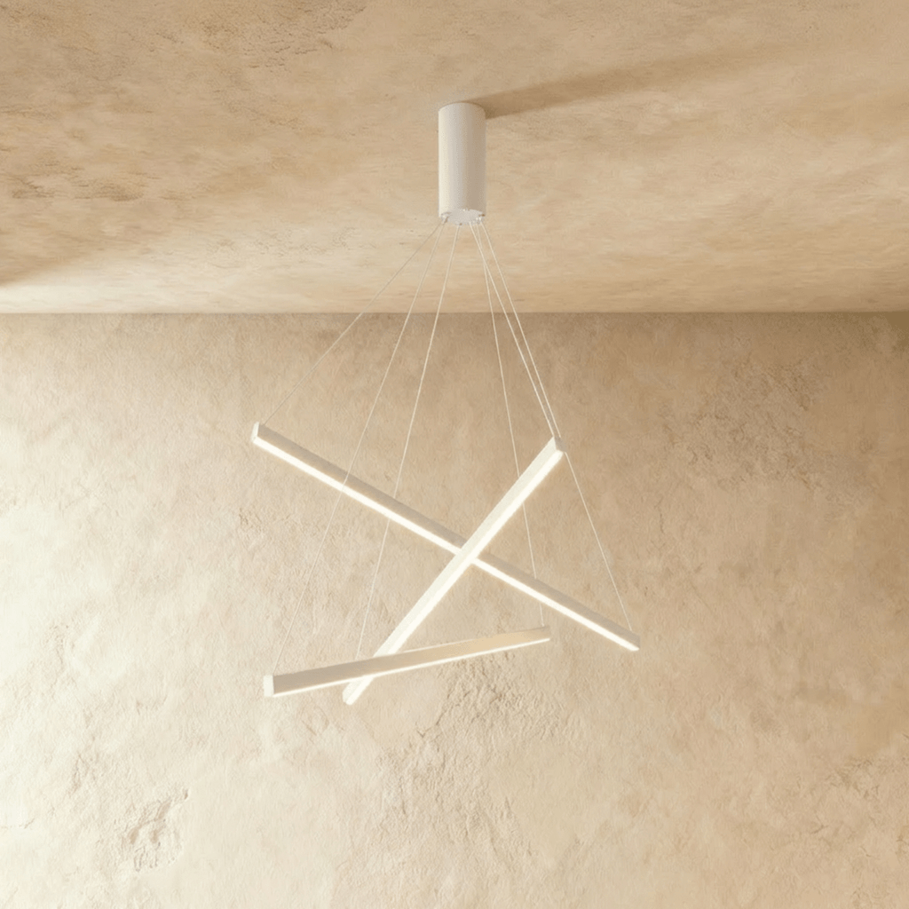 The Clérachic staggered chandelier in white aluminium, three crossed bars glowing warm white beneath a plastered ceiling.