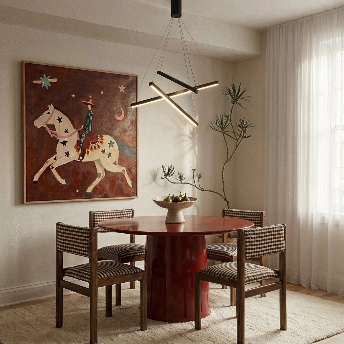 The Clérachic black staggered chandelier glowing warm white above a round red table in a dining room with a framed painting.