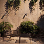 Two Clérachic black cylinder wall spotlights, switched off, mounted on a large-format stone wall above slatted chairs and a table.