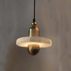 Clérachic black and gold pendant light, single alabaster disc on ribbed gold hardware, glowing on a white studio ground.