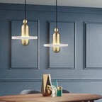 Clérachic single-disc pendants in gold hang as a pair over a round wood table against a blue paneled wall.