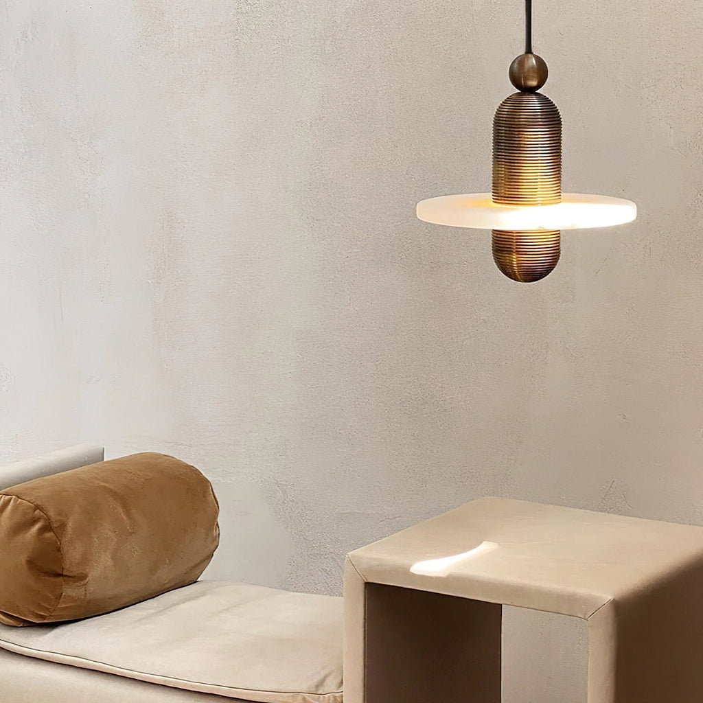 Clérachic gold single-disc pendant glowing above a cream daybed and tan side table on a plaster wall.