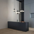 Clérachic single-disc pendants in black hang three-across over a matte black bar with glasses and a copper tray.