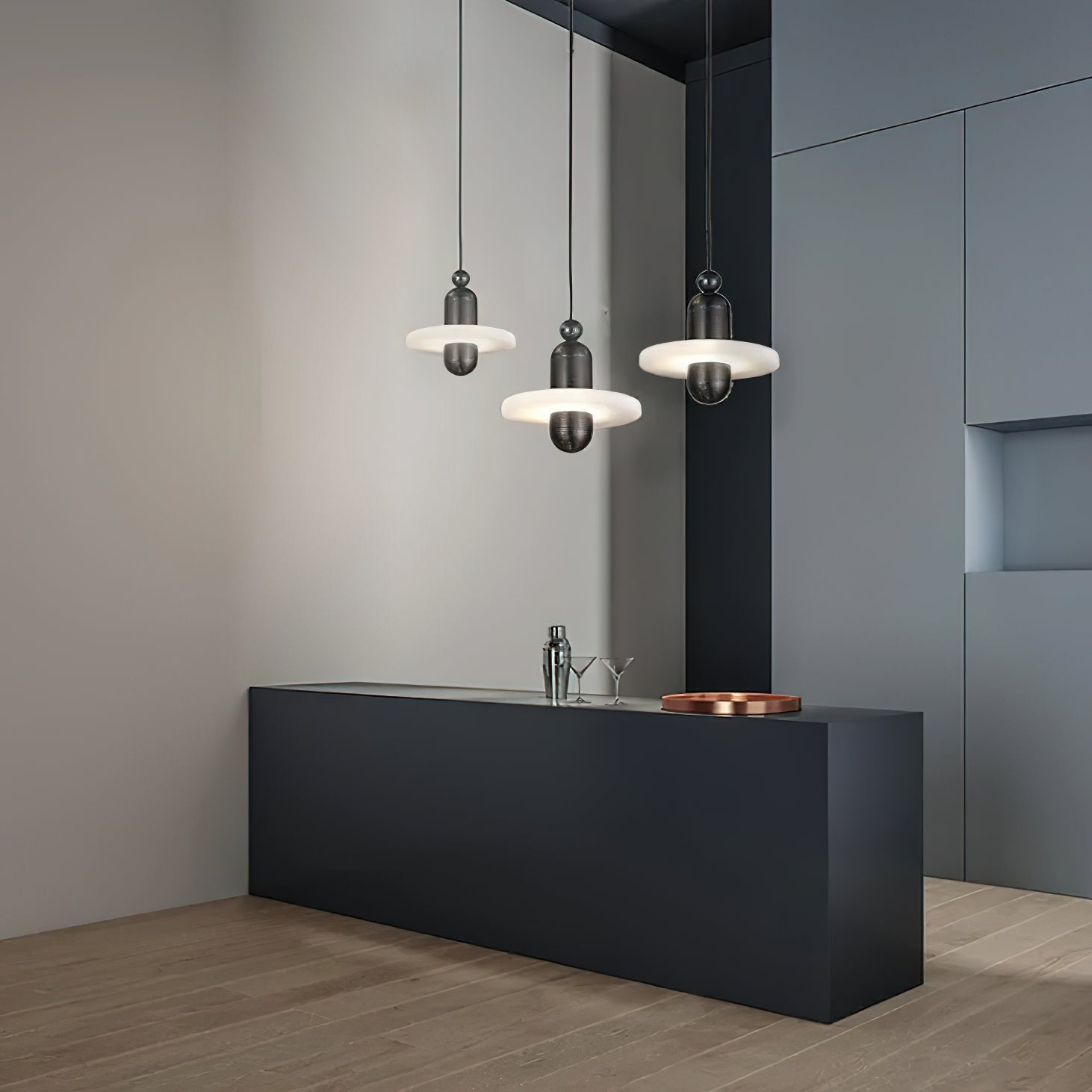 Clérachic single-disc pendants in black hang three-across over a matte black bar with glasses and a copper tray.