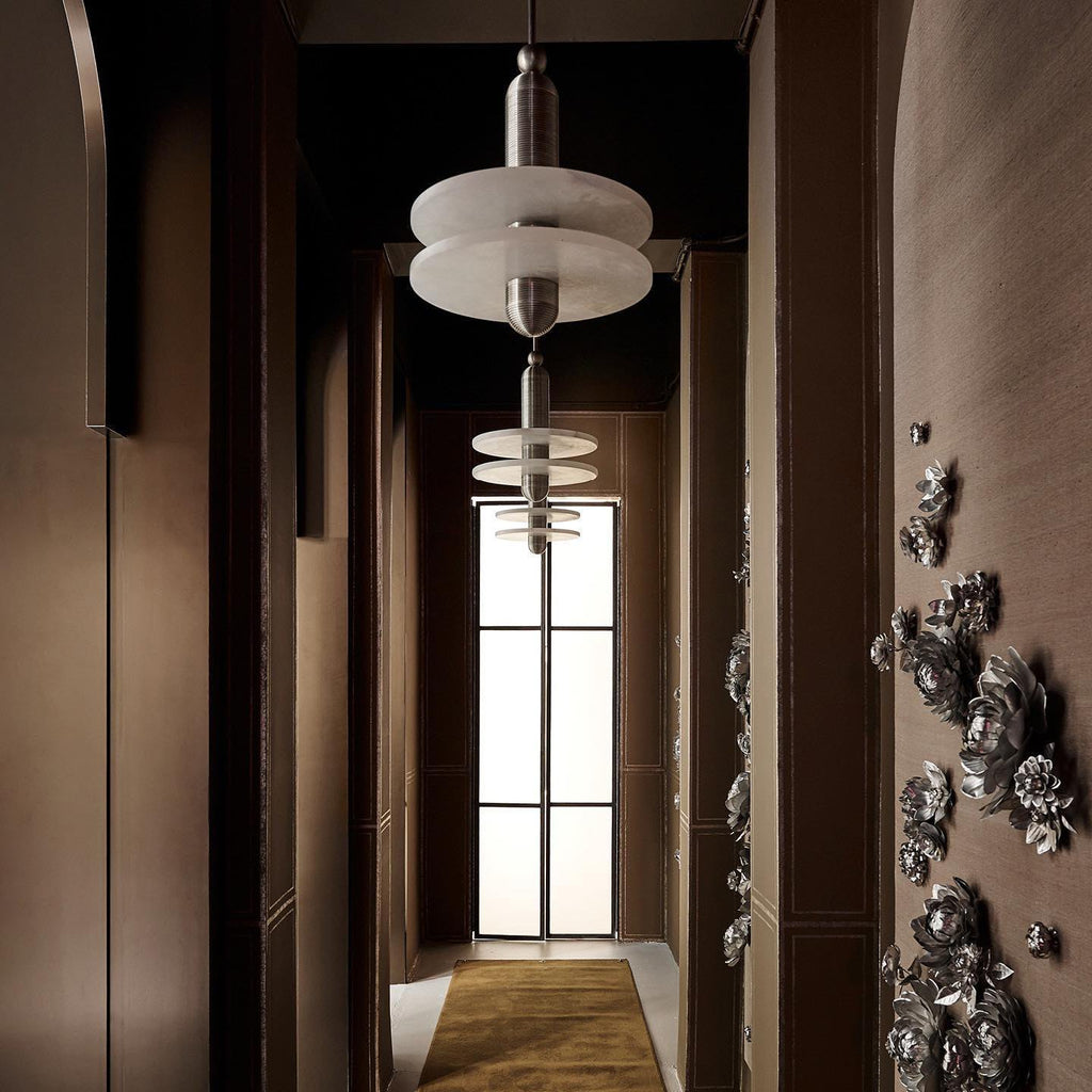 Clérachic double-disc pendants line a dark paneled hallway with a mustard runner toward a glass door.