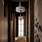 Clérachic double-disc pendants line a dark paneled hallway with a mustard runner toward a glass door.
