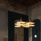 Clérachic gold double-disc pendants cluster four-high before a teal arched niche on a distressed plaster wall.