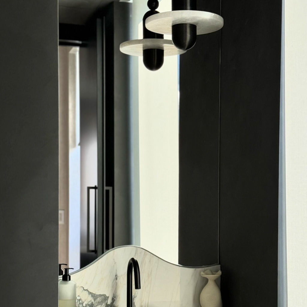 Clérachic single-disc pendants in black reflect in a tall bathroom mirror above a veined marble vanity.