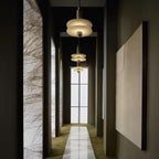 Clérachic gold double-disc pendants run three-down an olive hallway with a white marble runner.