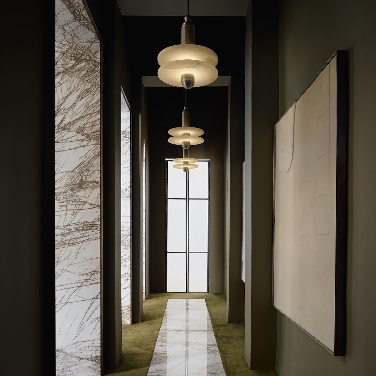 Clérachic gold double-disc pendants run three-down an olive hallway with a white marble runner.