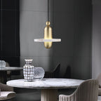 Clérachic gold single-disc pendant hangs over a round marble dining table in a charcoal-paneled room.