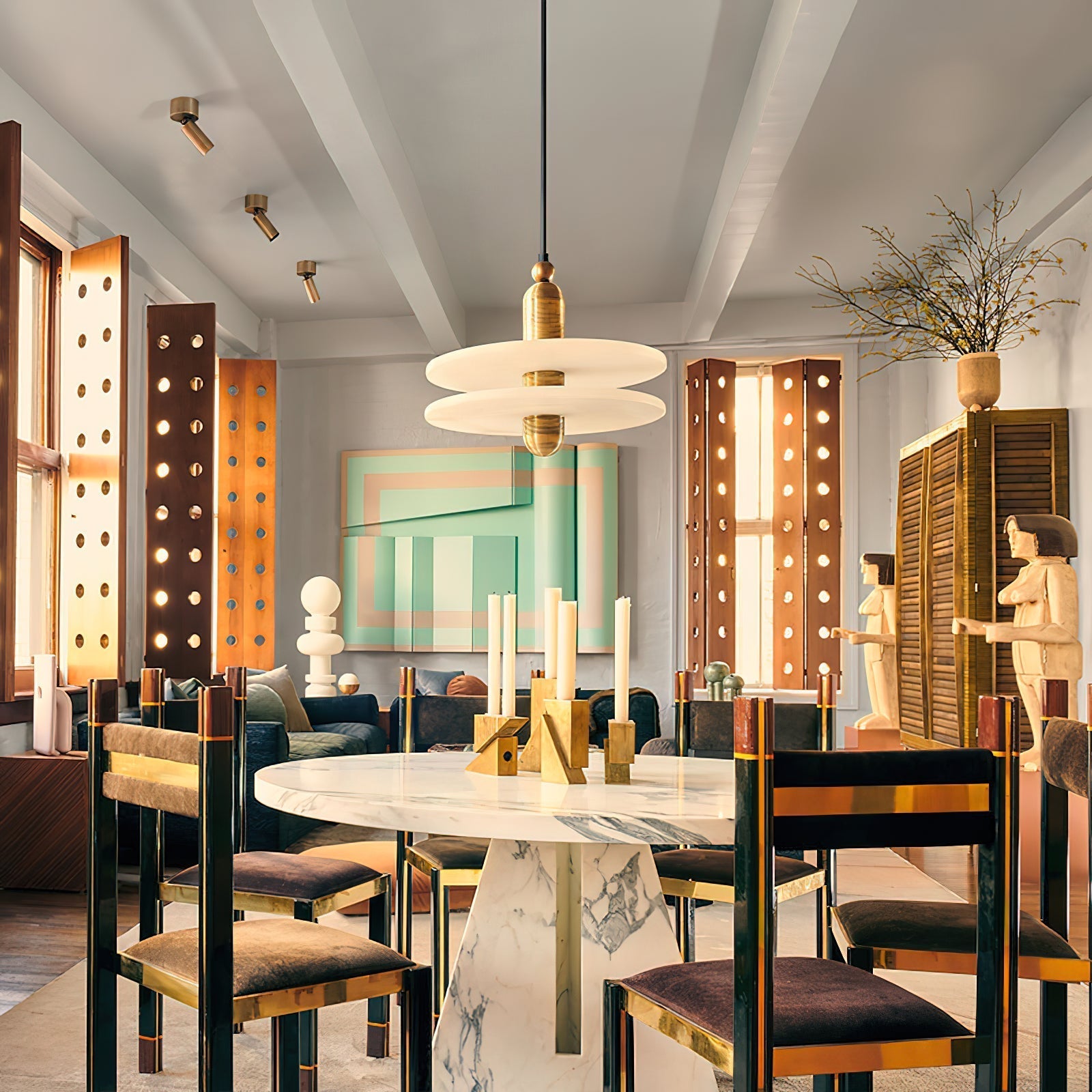 Clérachic gold double-disc pendant over a marble table, a geometric painting and circular-cut shutters behind.