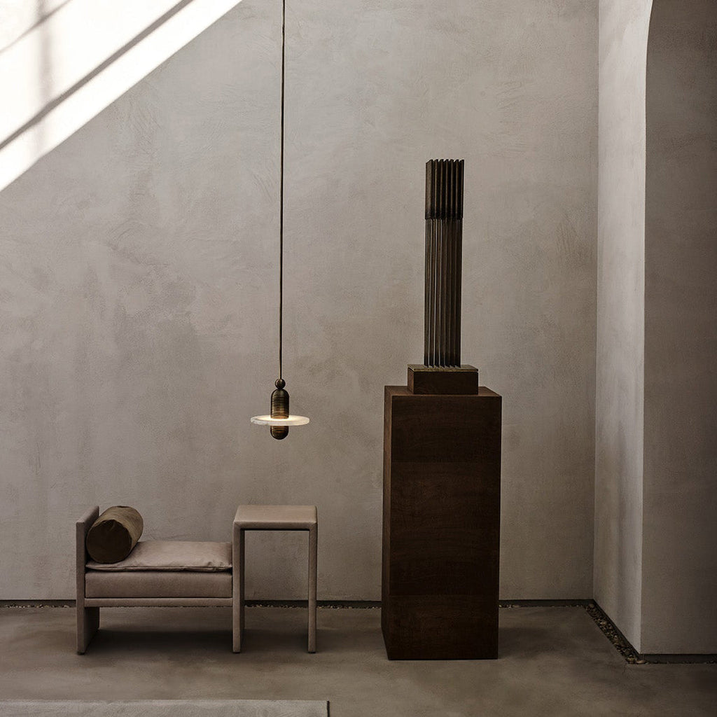 Clérachic black single-disc pendant glows beside a beige daybed as a sunbeam cuts across the plaster wall.