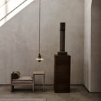 Clérachic black single-disc pendant glows beside a beige daybed as a sunbeam cuts across the plaster wall.