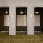 Clérachic gold double-disc pendants hang in marble-framed doorways along a green-carpeted gallery hall.