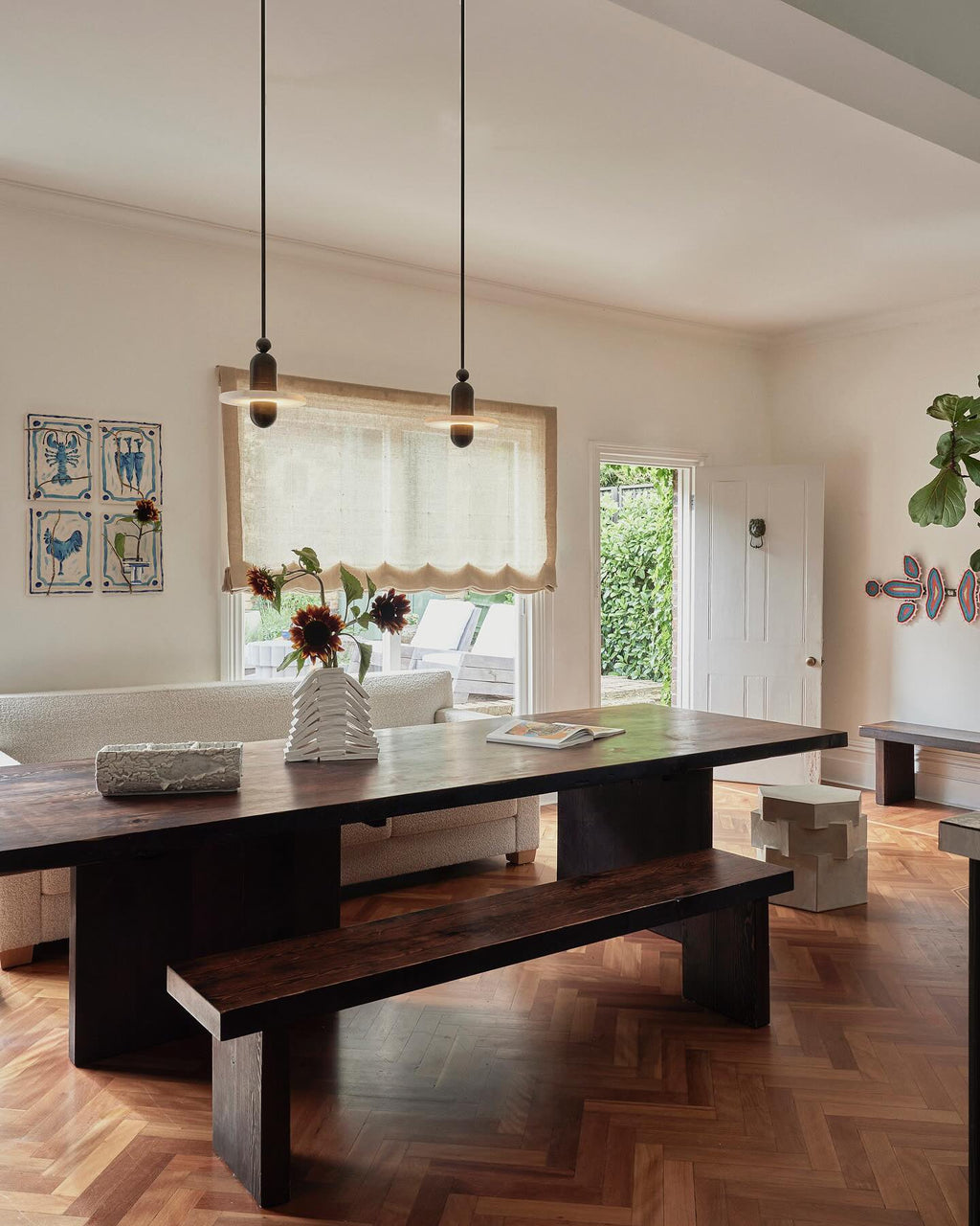 Clérachic black single-disc pendants hang over a rustic wood dining table by a door open to the garden.