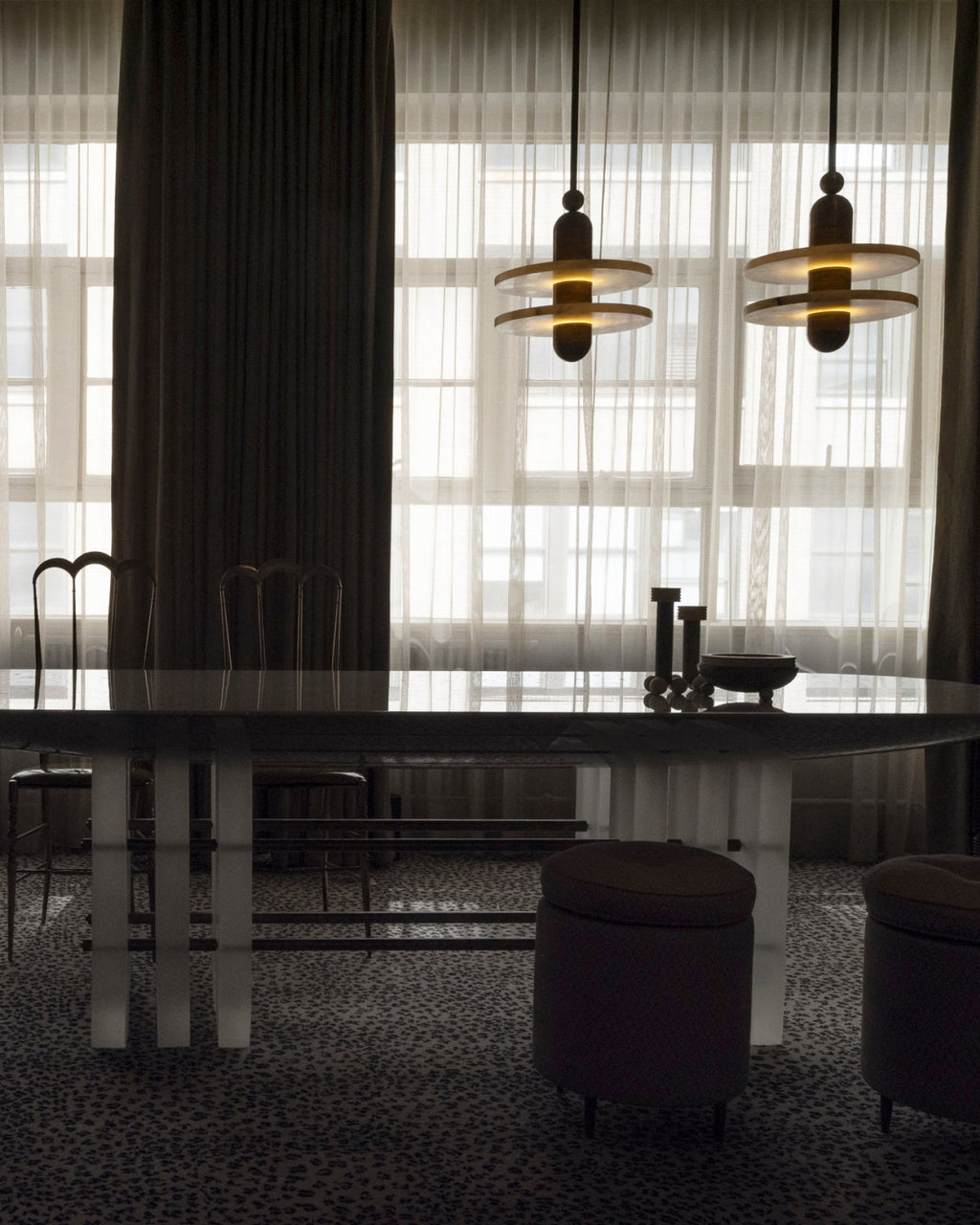 Clérachic double-disc pendants with black stems and gold-trimmed discs hang over a dark dining table.