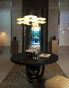 Clérachic gold double-disc pendants cluster seven-high over a round wood table facing a garden courtyard.