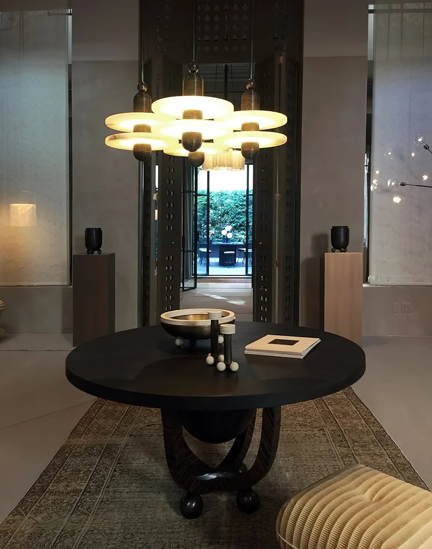 Clérachic gold double-disc pendants cluster seven-high over a round wood table facing a garden courtyard.