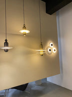 Clérachic pendants compared: black single-disc, gold single-disc, and gold double-disc on a cream wall.