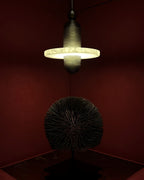 Clérachic black single-disc pendant glows in a deep red corner above a dark radiating sphere sculpture.