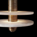 Clérachic gold double-disc pendant in close-up, ribbed gold stem lighting two veined alabaster plates.