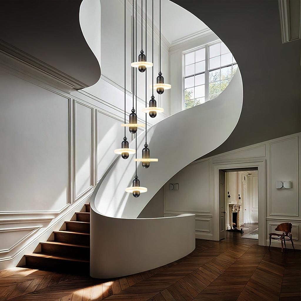Clérachic black single-disc pendants drop seven-high through a white spiral stairwell over herringbone floors.