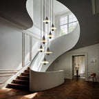 Clérachic black single-disc pendants drop seven-high through a white spiral stairwell over herringbone floors.