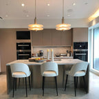 Clérachic gold double-disc pendants hang over a kitchen island with white stools and taupe handleless cabinets.