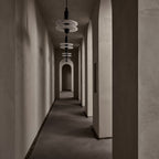 Clérachic pendants with stacked alabaster discs on black stems line a taupe arched hallway over pebbles.