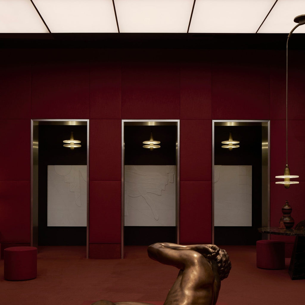 Clérachic gold double-disc pendants hang in red-paneled alcoves above a bronze reclining figure.