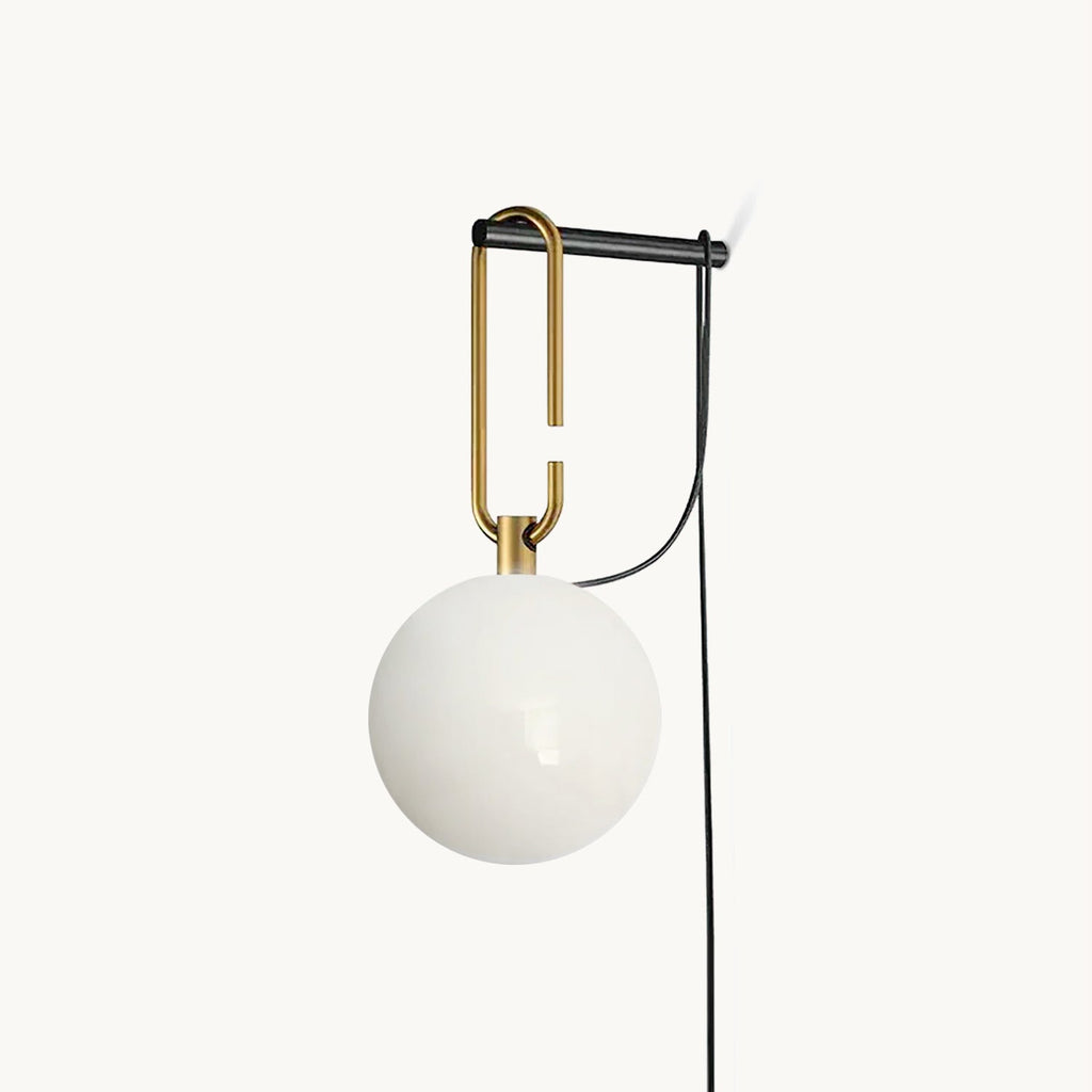 A Clérachic wall lamp with a frosted white glass globe hanging from a black and gold hook frame, its black cord looping down, on white.