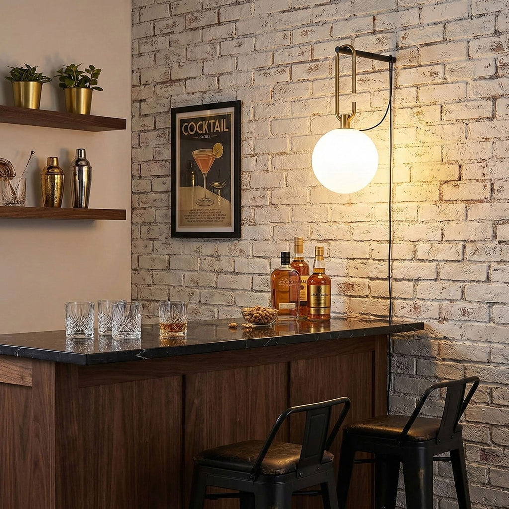 A glowing Clérachic globe wall lamp on a whitewashed brick wall, above a black-topped bar with bottles and a cocktail print.