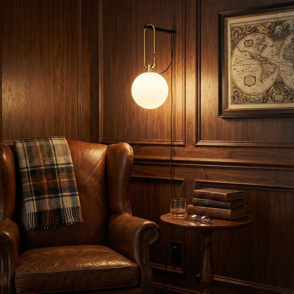 This Clérachic globe lamp glows warm on a dark wood-panelled wall, above a leather wing chair, a throw and a small round table.
