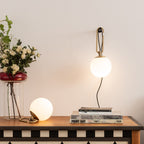 A lit Clérachic globe lamp hangs from a hook above a chequered console, with a small globe lamp and a stack of books below.