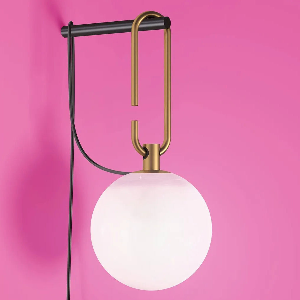 Close view of a white glass globe, the gold loop and black bar of this Clérachic wall lamp, against a bright pink wall.