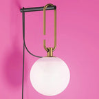 Close view of a white glass globe, the gold loop and black bar of this Clérachic wall lamp, against a bright pink wall.