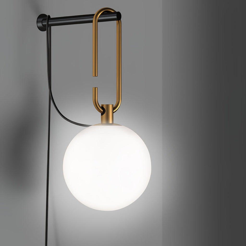 This Clérachic wall lamp glows white against a grey wall, its gold loop and black bar holding the frosted globe.