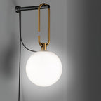 This Clérachic wall lamp glows white against a grey wall, its gold loop and black bar holding the frosted globe.