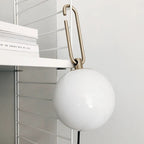 The gold hook of this Clérachic globe lamp hooked over a white shelving system, with books stacked on the shelf beside it.