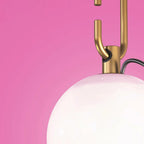 Close view of the gold loop and collar joining the black cord to the glass globe of this Clérachic lamp, on a pink wall.