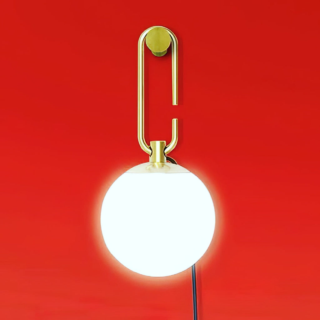A lit white globe on a gold loop, mounted to a round gold plate on a bold red wall, from Clérachic.