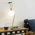 A small lit Clérachic globe wall lamp above a patterned wooden chest, a glass jug and a bowl, with a navy cushion at the right.