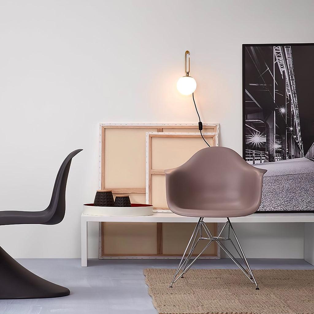 A small Clérachic globe wall lamp on a pale wall above a white bench with canvases, a mauve shell chair and a large black-and-white print.