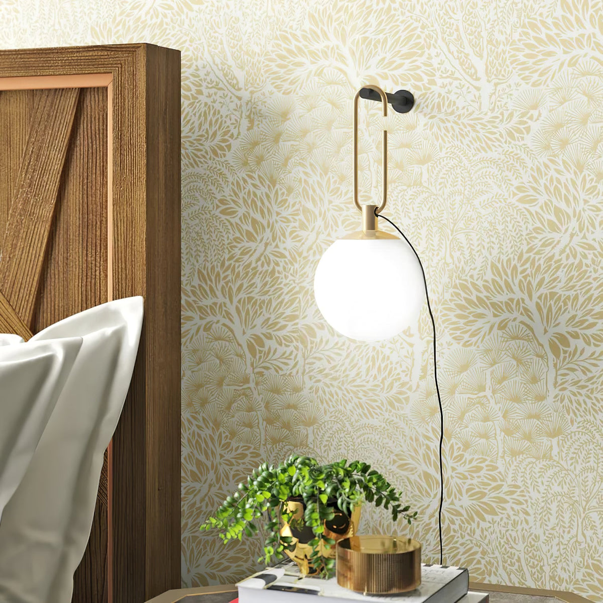 A Clérachic globe wall lamp on a cream floral wallpaper, beside a wooden headboard and a bedside stack with a plant and a brass bowl.